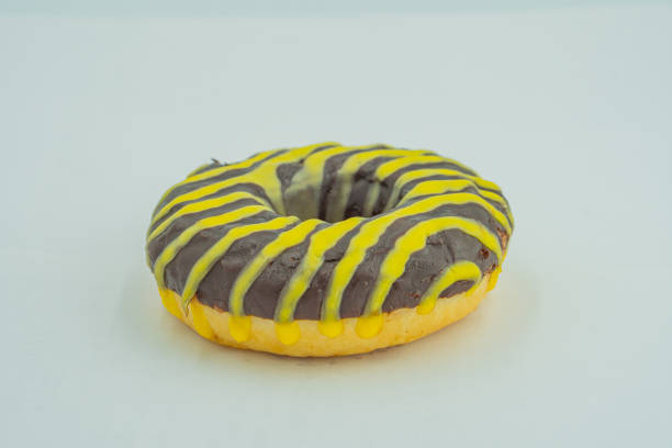 istock A single, freshly glazed doughnut with a contrasting chocolate and vanilla frosting pattern, adorned with yellow and green stripes The image is captured in a straightforward style against a neutral 2197088222