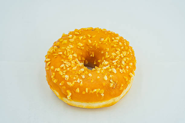 istock A single, vibrant yellow doughnut with orange seeds or nuts on a light gray surface The focus is solely on the doughnuts appearance and texture 2197088233