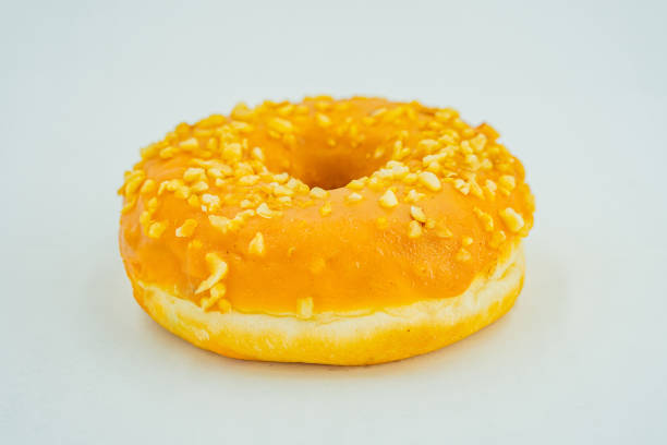 istock A single, fresh-looking, yellow-glazed doughnut with seed or nut specks sits on a light surface against a neutral backdrop 2197088249