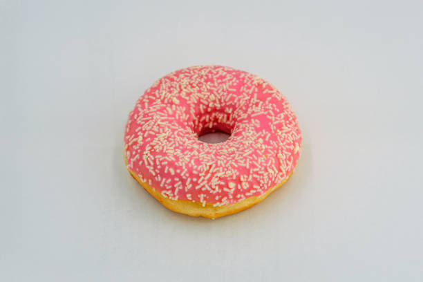istock A vibrant, close-up image of a single pink frosted doughnut adorned with multicolored sprinkles on a speckled white surface 2197088266