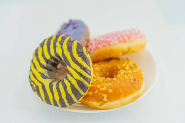 istock Image of a plate with three doughnuts, each decorated differently one striped yellow and purple, another plain, and the third dusted with orange sprinkles The plate has a reflective surface, and th 2197088295