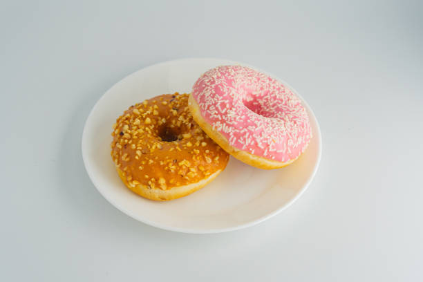 istock Three doughnuts with different toppings nut-covered glaze, pink sprinkles on a white plate resting on gray surface Photo highlights doughnut textures 2197088403