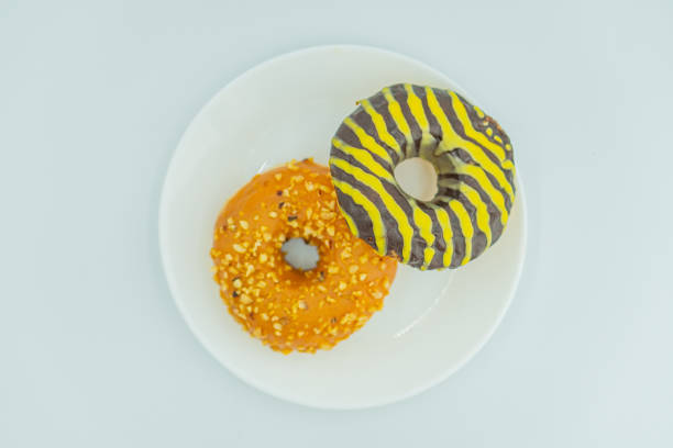 Image shows a plate with three doughnuts, each with unique toppings One plain, another orange with specks, and the last striped like a bumblebee
