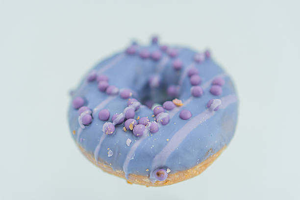 Image of a single blue-glazed doughnut with purple speckles, placed against a neutral backdrop