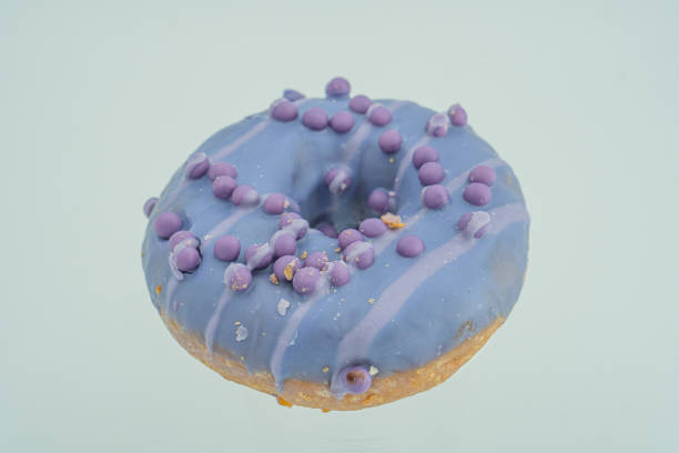 istock A single, glossy purple doughnut with a textured blue-speckled glaze is the central focus of this image against a soft, neutral background 2197088539