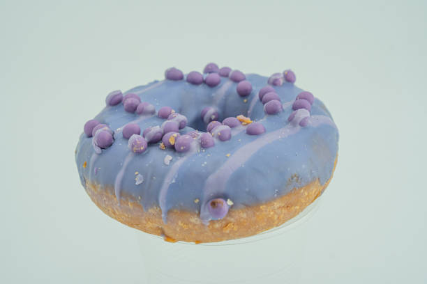 istock Image shows a single round doughnut with lavender icing, artistically swirled or drizzled It has contrasting spherical confectionery balls and is set against a plain background The style suggests c 2197088552