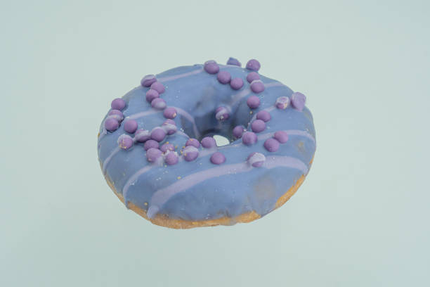istock A single purple doughnut with vibrant sprinkles on a light gray surface, against a white background 2197088554