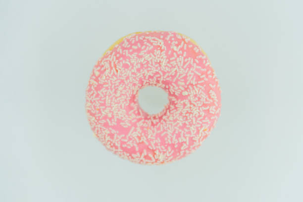 Image features a single, pink-frosted doughnut with sprinkles against a neutral backdrop, likely for culinary presentation or advertising