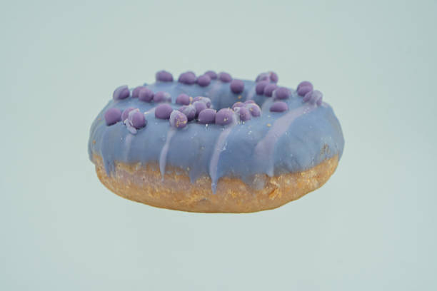 istock Image of a single, blue-glazed doughnut on a light grey background with gold-brown base and purple sugar bits as decoration 2197088584
