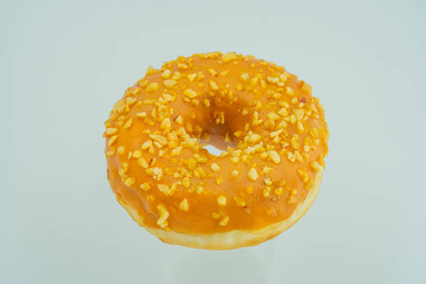istock A single, central donut rests on a light grey surface, glazed orange with nuts sprinkled Simple lighting emphasizes the sweet treats appearance 2197088698