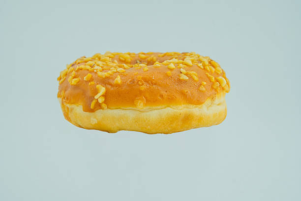 istock Image shows a contrasting, glossy golden-brown doughnut on a light blue background, possibly topped with seeds or sugar 2197088729