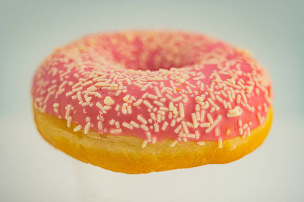 istock Close-up view of a single, slightly textured doughnut with pink icing and contrasting toppings possibly nuts or seeds, shot with shallow depth of field 2197088864