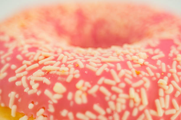 A close-up image of a fresh, pink glazed doughnut with complementary sprinkles a