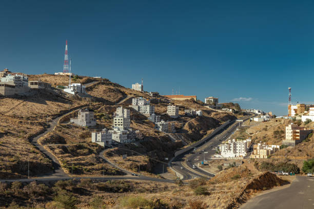 Skyline of Abha, Saudi Arabia.A stunning panoramic view of Abha, the capital city of the Asir Region in Saudi Arabia. Nestled in the mountains, Abha is known for its cool climate, unique architecture, and breathtaking landscapes. The image captures the city's vibrant mix of modern and traditional buildings, with a mosque's minaret standing out in the foreground. Rolling hills and industrial structures in the distance add depth to this picturesque urban scene. High-quality photo