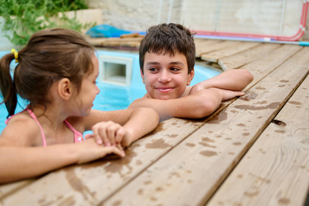 Two children are relaxing near a pool, smiling and enjoying their playful outdoor time. Their vibrant energy and bond highlight the joys of childhood during a sunny summer day.