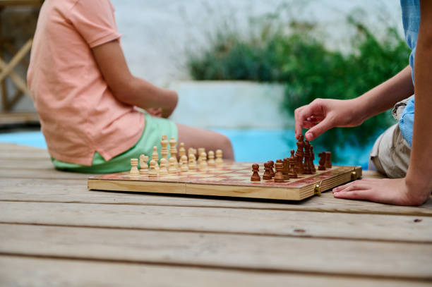 istock Children playing chess outdoors on a wooden deck by a swimming pool 2197092475