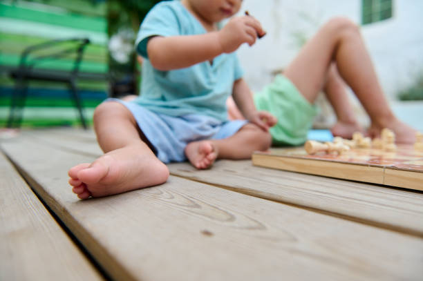 Children enjoying a strategic chess game on a wooden deck in the backyard. Captures a sunny outdoor activity showcasing focus and leisure with vibrant surroundings. Perfect for themes of childhood, strategy, or outdoor games.