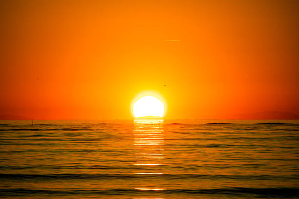 A golden sunset over the sea, with an orange sun in the center, its reflection shining on the calm water.