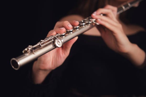 istock Musician's hands holding and playing a silver flute on a dark background. Studio music photography. Classical performance and wind instrument concept. 2197094653