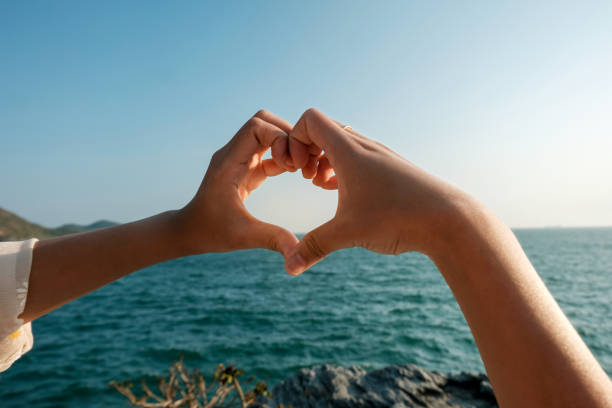 Hands Forming A Heart Shape Against A Serene Ocean Horizon. Romantic Gesture Symbolizing Love, Togetherness, And Freedom. Perfect For Couples, Vacations, Honeymoon, Wedding, And Summer Travel Concepts.