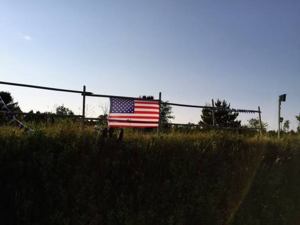 An American Flag on a fence in a field near a bicycle trail.