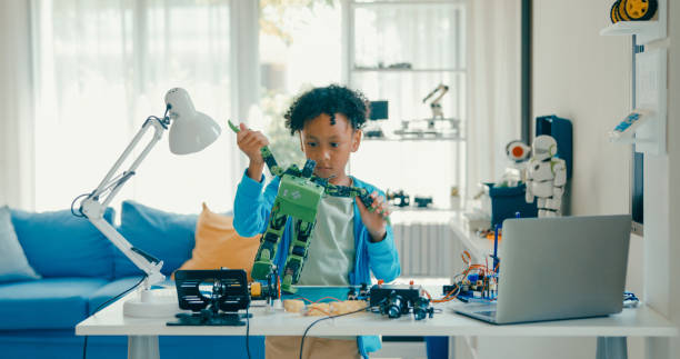 istock Young African-American boy meticulously assembles and adjusts robotic arm, showcasing his engagement with STEM learning in home workshop. STEM Education robotics courses online. 2197102676