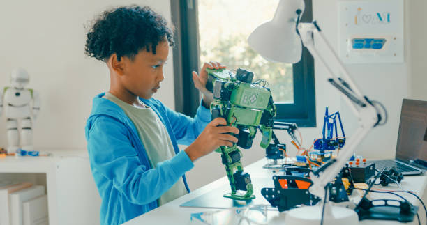 istock Young African-American boy meticulously assembles and adjusts robotic arm, showcasing his engagement with STEM learning in home workshop. STEM Education robotics courses online. 2197102683