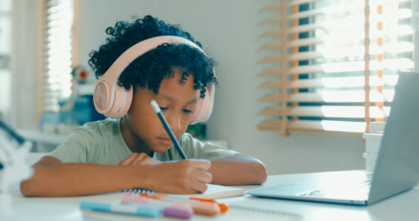 istock Young African-American boy wearing headphones, is deeply focused while participating in online learning session from home. Education courses online. 2197102705