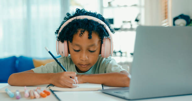 istock Young African-American boy wearing headphones, is deeply focused while participating in online learning session from home. Education courses online. 2197102709