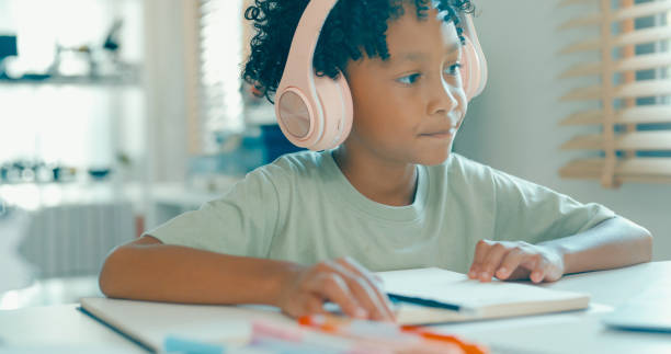 istock Young African-American boy wearing headphones, is deeply focused while participating in online learning session from home. Education courses online. 2197102710