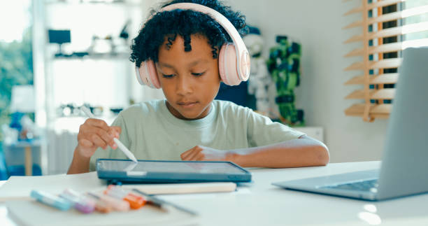 istock Young African-American boy uses digital tablet and stylus for schoolwork while participating in e-learning session at home. Education courses online. 2197102712