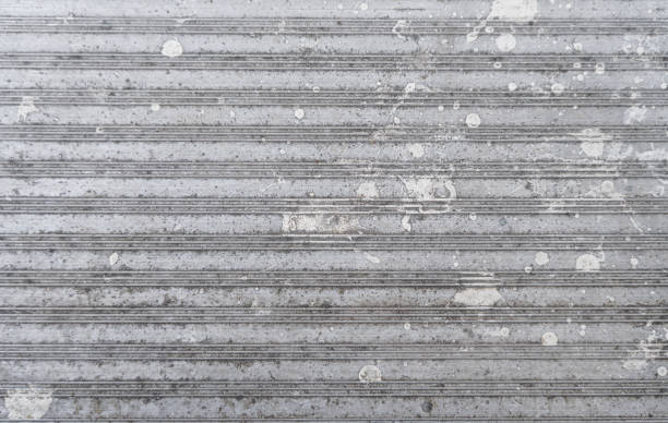 Close-up of a grey metal sheet with horizontal lines and scattered white splotches. Shows signs of wear and weathering.