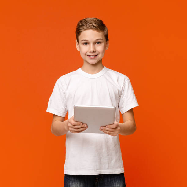 istock Teen boy using digital tablet on orange studio background 2197107490