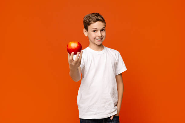 istock Positive little boy offering fresh red apple on camera 2197107515