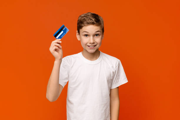 istock Cute boy holding credit card, orange studio background 2197107518