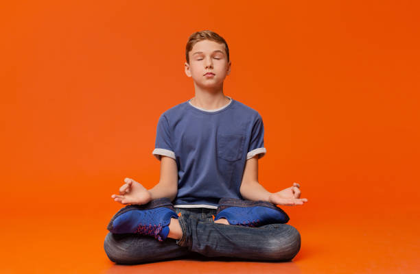 istock Calm boy sitting on floor and meditating in lotus position. 2197112068