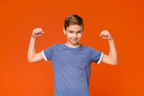 istock Cute boy showing biceps on orange background 2197112075
