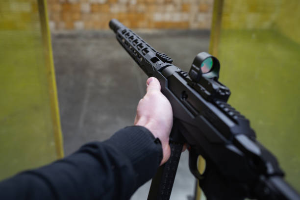 Modern tactical rifle in 9mm caliber with a silencer and red dot sight in shooter hands, first person view.