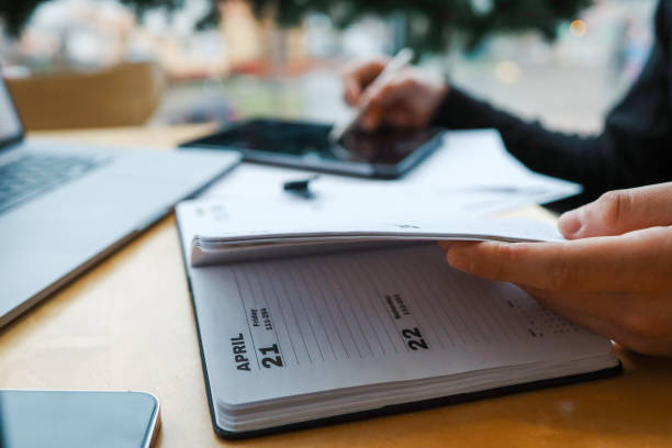 A professional workspace with a person organizing tasks using a notebook, tablet, and laptop on a wooden table, creating a productive and modern office environment.
