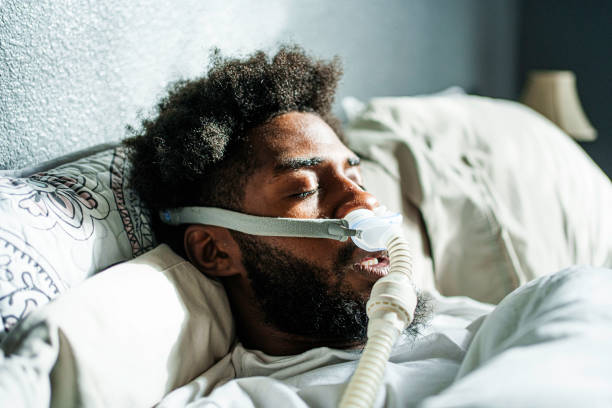 istock Young African American Man in His Twenties Sleeping Soundly Using a CPAP Machine for Sleep Apnea 2197120088