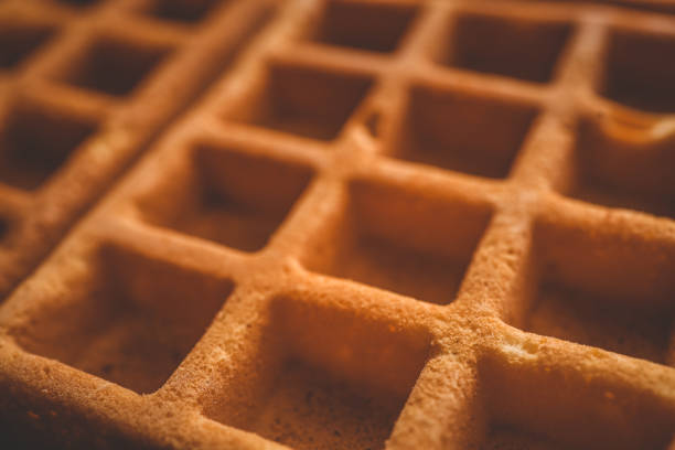 Golden-brown crispy waffles in a close-up shot. Detailed texture with a crisp outer layer and soft interior. Freshly baked breakfast food with a warm and inviting appearance.