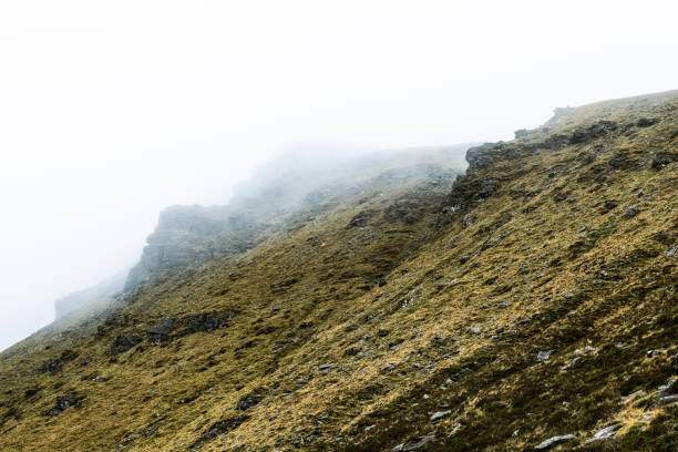 istock A mist envelops a mountain range, highlighting rugged cliffs and gentle slopes. The lush green terrain glistens, showcasing nature's tranquility in early morning light. 2197121350