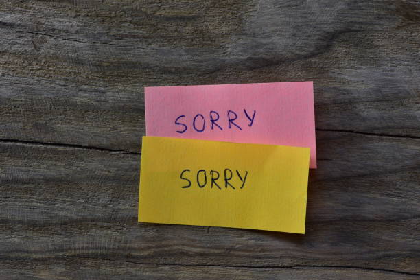 istock Message sorry on pink and yellow sticky notes on wooden board textured background. A pen wrote word sorry on note papers. 2197121529