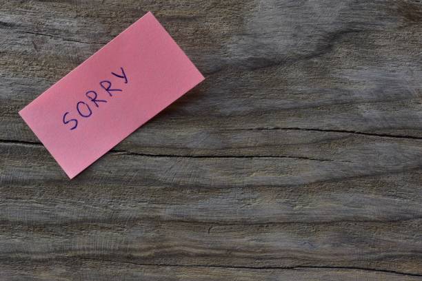 istock Message sorry on pink sticky note on wooden board textured background. A pen wrote word sorry on note paper. 2197121702