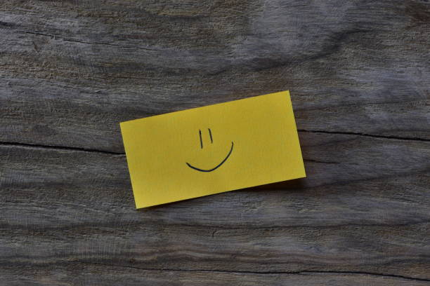 istock Smiley face on yellow sticky note on wooden board textured background. A pen draw smiley face on note paper. 2197122049