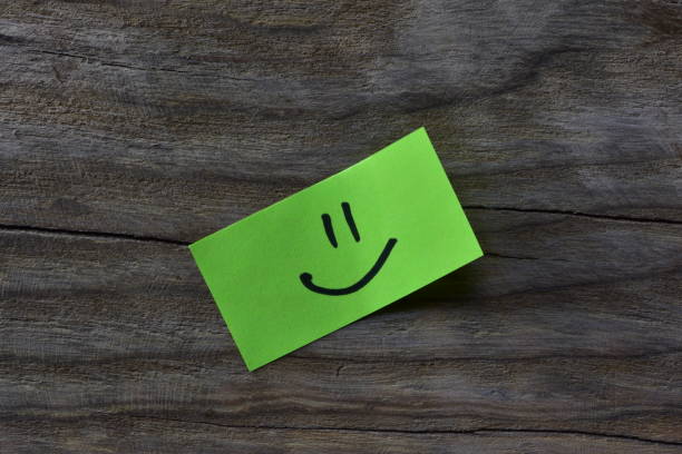istock Smiley face on green sticky note on wooden board textured background. 2197122344