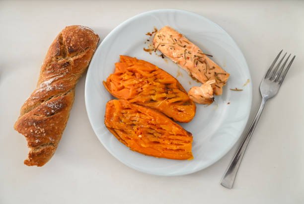 A comforting meal features tender salmon fillet and roasted sweet potatoes beside a crusty bread roll.