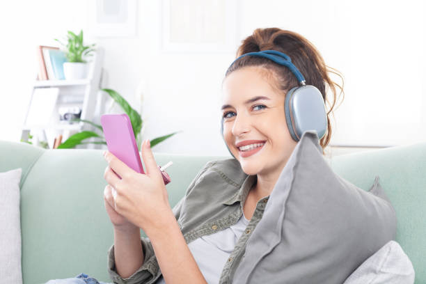 istock Young, smiling woman on couch vaping with an electronic cigarette vape device , holding smartphone while browsing messages, social media, and digital content, wearing headphones and listening to music 2197124684