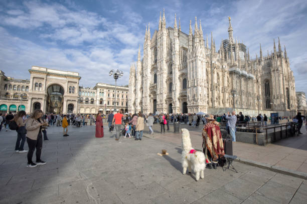 Duomo di Milano at Piazza del Duomo filled with tourists, Milan, Italy on a sunny afternoon. A music performer with a llama standing aside.
