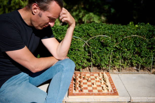 Man thinking deeply while playing an outdoor chess game on a sunny day